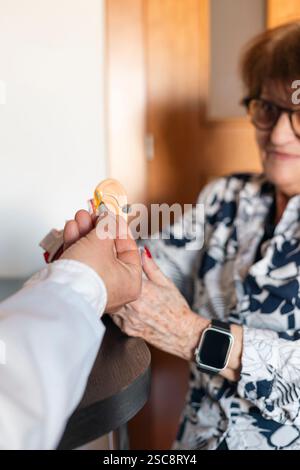 Arzt, der einer älteren Patientin während der ärztlichen Beratung erklärt, wie Hörgerät funktioniert Stockfoto