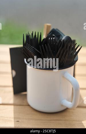 Eine Sammlung von Gabeln und verschiedenen Besteck, die in einem weißen Becher auf einem Tisch angeordnet sind Stockfoto