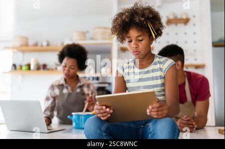 Glückliche afrikanische Familie, die Spaß mit dem Gerät zu Hause hat, indem sie ein digitales Tablet verwendet, das gemeinsam auf den Bildschirm blickt Stockfoto