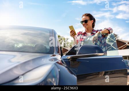 Frau, die auf den Bildschirm des Mobiltelefons blickt, während sie draußen neben ihrem Auto steht Stockfoto