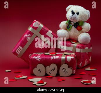Geschenkboxen mit einem Teddy auf rotem Hintergrund mit kleinen Herzen Stockfoto