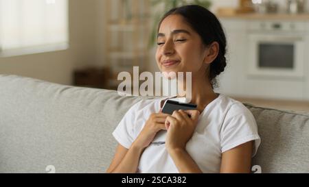 Glücklich aufgeregt Freude Arabische Frau indische Mädchen Dame Frau zu Hause auf Couch Shopping Online Kreditkarte Bank Handy erfolgreiche Zahlung Dome Stockfoto