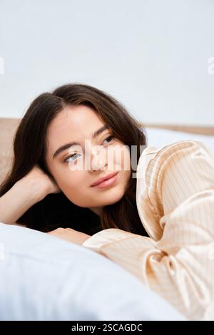 Eine junge Frau entspannt sich auf einem weichen Bett, verloren in einer beruhigenden Atmosphäre. Stockfoto