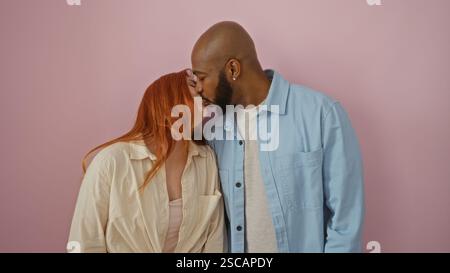 Interrassisches Paar teilt liebevollen Kuss vor isoliertem rosa Hintergrund, der Zuneigung und Verbindung demonstriert Stockfoto