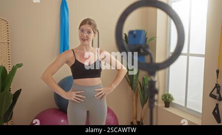 Die blonde Frau nimmt sich in einem Fitnessstudio auf, mit Bälle und Fitnessgeräten im Hintergrund Stockfoto
