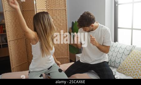 Paare tanzen spielerisch auf dem Bett in gemütlichem Wohnraum, fröhlicher Mann und Frau, die gemeinsam in Innenräumen mit hellem natürlichem Licht Spaß genießen Stockfoto