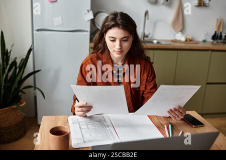 Eine Frau sitzt an einem Tisch, umgeben von Papieren, und reflektiert ihre Gefühle in einer gemütlichen Küche. Stockfoto