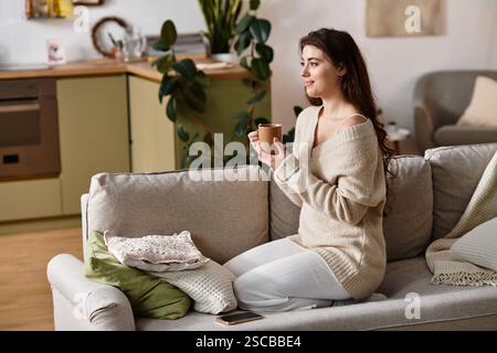 In einem warmen und gemütlichen Wohnzimmer denkt eine Frau über ihre Gefühle nach, während sie eine Tasse Tee genießt. Stockfoto