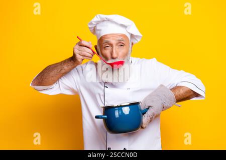 Älterer männlicher Koch in weißem, einheitlichem Essen mit leuchtendem gelbem Hintergrund Stockfoto