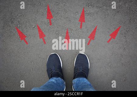 Mann, der neben roten Pfeilen auf Asphaltstraße steht, Nahaufnahme. Konzepte der Wahl, der Entscheidung, der anderen Art und Weise, der Alternative Stockfoto