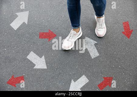 Frau, die auf Asphaltstraße läuft, mit roten und weißen Pfeilen, die in verschiedene Richtungen zeigen, Nahaufnahme. Konzepte der Wahl, der Entscheidung, des alternativen Weges Stockfoto