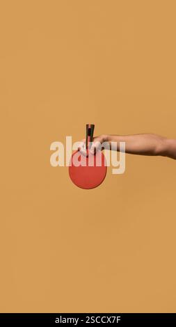 Die Hand dehnt das rote Tischtennispaddel horizontal aus und veranschaulicht die Kontrolle und Manövrierbarkeit im professionellen Tischtennis vor beigefarbenem Hintergrund. Stockfoto
