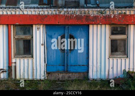Verlassenes Industriehaus mit blauen Doppeltüren und Fenstern auf beiden Seiten, altes Bäckereigebäude aus Wellblech Stockfoto