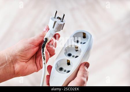 Verbrannter Stecker und Steckdosenleiste in der Hand gehalten. Stockfoto