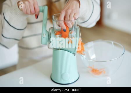 Weibliche Hand hackt Karotten auf dem Boden mit einer automatischen blauen Reibe Stockfoto