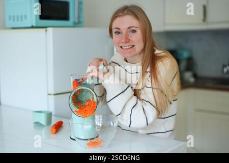 Mädchen zu Hause Küche hackt Karotten auf dem Boden mit einer automatischen blauen Reibe Stockfoto