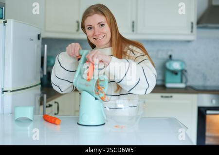 Mädchen hackt Karotten auf dem Boden mit einer automatischen blauen Reibe Stockfoto
