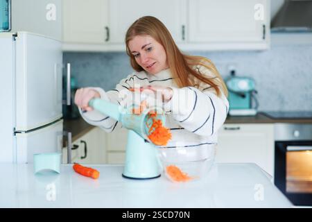 Mädchen in der Küche zubereiten frischen Salat und hackt Karotten auf dem Boden mit einer automatischen blauen Reibe Stockfoto