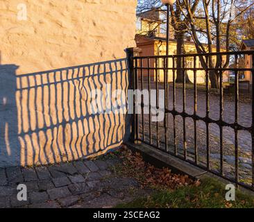 Ein schmiedeeiserner Zaun wirft komplizierte Schatten auf eine Steinmauer in einem sonnendurchfluteten Innenhof. Stockfoto