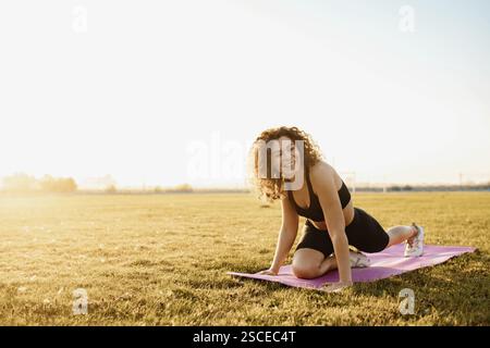 Frau lächelt beim Yoga auf einer Matte in einem hellen Feld Stockfoto