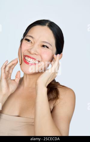 Glückliche asiatische Frau mittleren Alters lacht. Anti Age Gesichtspflege und Schönheit. Stockfoto