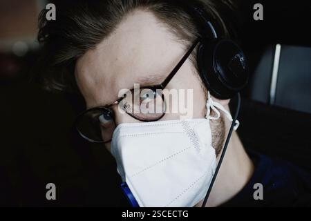 Ein Mann mit Brille, Maske und Kopfhörern scheint drinnen konzentriert zu sein Stockfoto