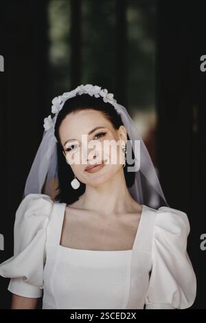 Eine lächelnde Frau in einem Brautkleid und Schleier mit Blumendetails Stockfoto