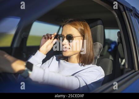 Frau, die Sonnenbrille in einem Auto trägt und sie mit einer entspannten Atmosphäre anpasst Stockfoto