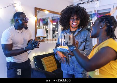 Multi-ethnische Freunde überraschen einen Mann mit Geburtstagskuchen zu Hause während der Nachtparty Stockfoto