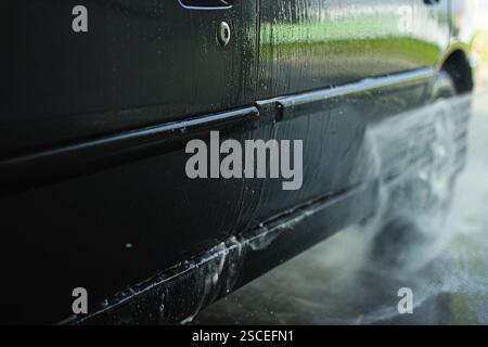 Nahaufnahme eines schwarzen Autos beim Waschen mit sichtbarem Wasserstrahl Stockfoto