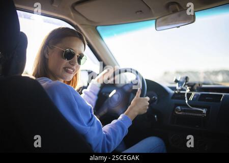 Lächelnde Frau in einem Auto, die das Lenkrad hält, Sonnenbrille trägt Stockfoto