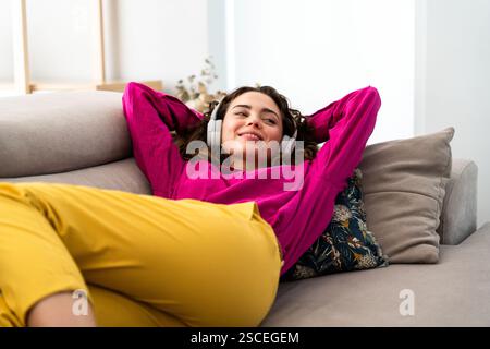Schöne junge Frau, die sich auf dem Sofa entspannt und Musik mit Kopfhörern zu Hause hört - fröhlich hübsche weibliche Erwachsene, die eine gute Zeit zu Hause verbringen Stockfoto