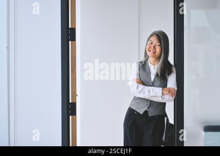 Asiatische Geschäftsfrau mittleren Alters, die im Büro steht. Hochformat. Stockfoto