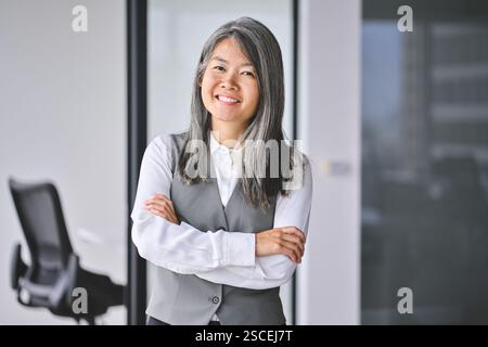 Reife asiatische Geschäftsfrau, die im Büro steht und auf Kamera und Porträt blickt. Stockfoto