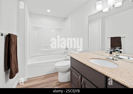 Ein Badezimmer mit einer weißen Toilette und einem braunen Handtuch, das an der Wand hängt. Das Bad ist sauber und gut beleuchtet Stockfoto