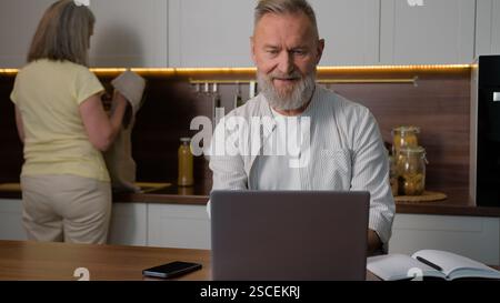 Ältere kaukasische Familie in der Küche Mann mittleren Alters Mann im Ruhestand Geschäftsmann Fernarbeit Fernunterricht online von zu Hause aus mit Laptop Computer Stockfoto