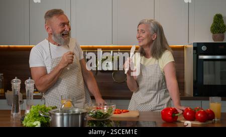 Lustiges weißes Paar verliebt reife ältere ältere ältere Frau mittleren Alters und Ehemann im Ruhestand verheiratete Familie sang fröhlich bei Löffeln Küchengeschirr Stockfoto