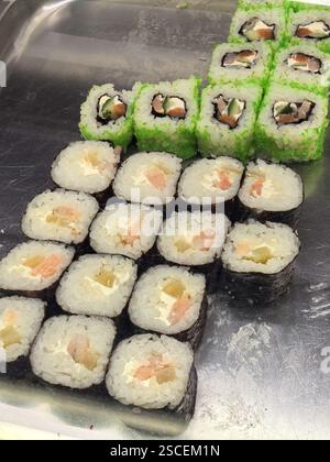 Farbenfrohe Sushi-Rollen sind kunstvoll auf einer Oberfläche aus Edelstahl angeordnet und präsentieren frische Zutaten. Der grüne und schwarze Reis stehen im Kontrast zu Shar Stockfoto
