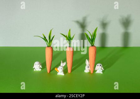 Karotten mit kleinen weißen Häschen auf grauem und grünem Hintergrund. Minimales Osterkonzept. Minimale Zusammensetzung der Feder. Stockfoto
