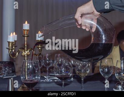 Rotwein von Hand aus der Karaffe in Weingläser vor Messingkandelabern gießen. Stockfoto