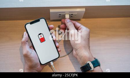 Mann Hand, der das Ladegerät im Café an das Smartphone anschließt, natürliches Morgensonnenlicht. Nahaufnahme eines Mannes, der ein Smartphone hält, das mit einer Ladung verbunden ist Stockfoto