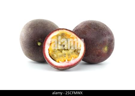 Zwei ganze Passionsfrüchte und eine Hälfte, die das gelbe Fruchtfleisch mit den schwarzen Samen zeigen, liegen auf weißem Hintergrund, die Haut ist violett und die Früchte a Stockfoto