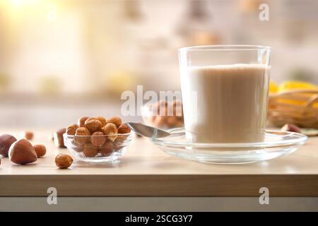 Glasbecher gefüllt mit alternativem pflanzlichem Haselnussgetränk mit Haselnussschalen auf hölzerner Küchenbank. Vorderansicht. Stockfoto