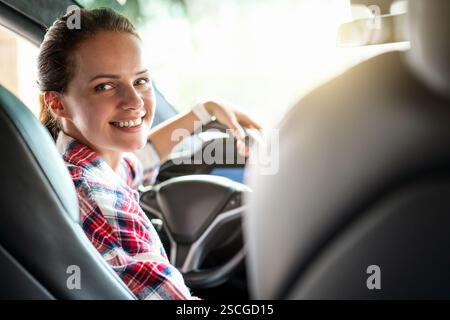 Junge Frau auf dem Fahrersitz, die mit einem Lächeln in die Kamera zurückblickt Stockfoto