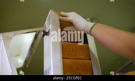 Ein Brotlaib wird auf ein Förderband gelegt. Frisches Brot für die Herstellung von Crackern. Stockfoto