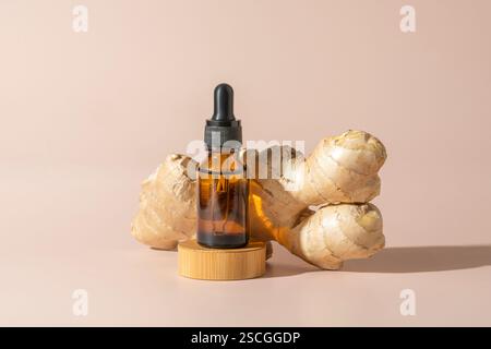 Ein Gesichts- oder Haarserum oder ätherisches Öl in einer braunen Tropfflasche mit Ingwerextrakt, das auf einem hölzernen Podium steht Stockfoto