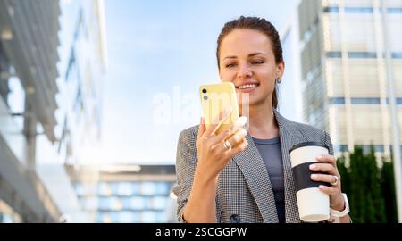 Geschäftsfrau draußen auf der Stadtstraße, die ihr Smartphone ansieht und lächelt Stockfoto