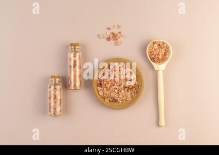 Ein Holzlöffel und Glasbootles mit rosafarbenem Salz für Körperbehandlungen oder Spa-Behandlungen auf beigefarbenem Hintergrund Stockfoto