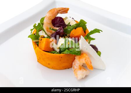 Frische Garnelen ruhen auf einem lebendigen Salat mit gemischtem Gemüse, Kürbis, Fetakäse und Oliven, elegant auf einem hellen weißen Teller, hochglänzend Stockfoto