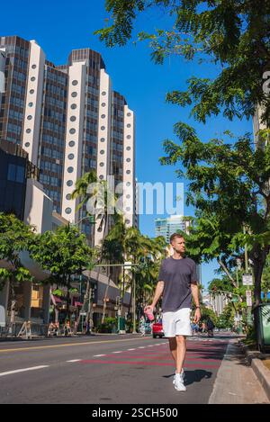 Mann, der entlang der Palm Linked Street mit Hochhäusern in Honolulu läuft Stockfoto